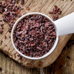 Spoonful of pure cacao nibs – rustic wooden background